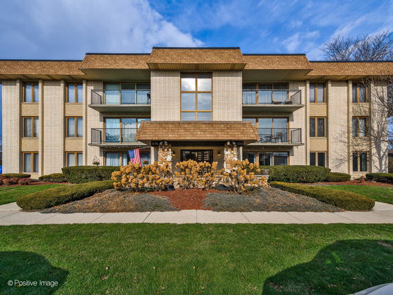 Front view of a multi-story apartment building with balconies and a central entrance.