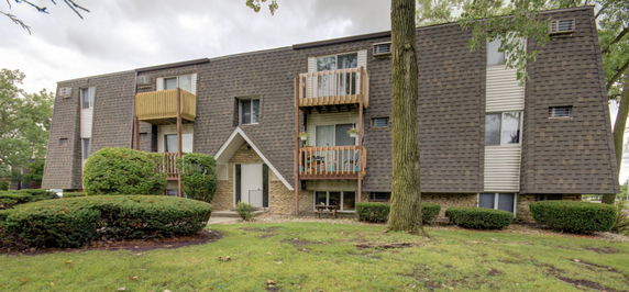Front view of a multi-story residential building with small balconies and a gabled entrance.