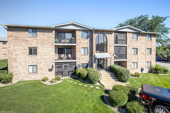 Front view of a three-story brick apartment building with balconies.
