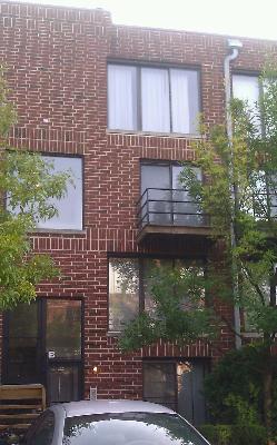 Front view of a brick multi-story building with windows and a small balcony.