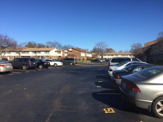 Outdoor parking area with multiple parked cars in front of residential buildings.