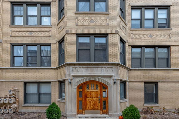 Front view of a multi-story brick building with wooden entrance door and large windows.