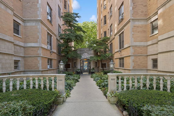 Front view of a multi-story brick building with a central entrance and landscaped walkway.