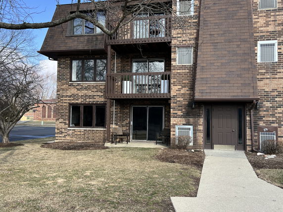 Front view of a multi-story brick apartment building with balconies and a shingled roof section.