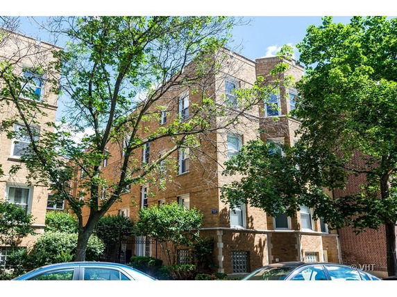 Front view of a multi-story brick building with trees and parked cars in front.
