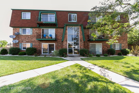 Front view of a three-story brick apartment building with balconies and a central entrance.