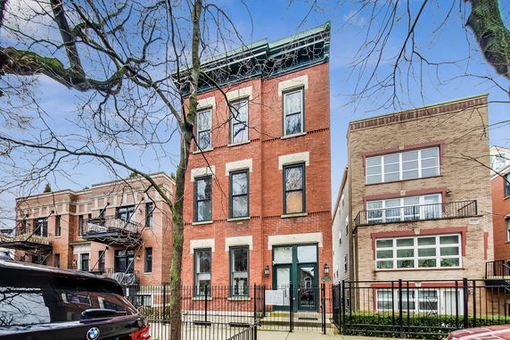 Front view of a three-story red brick townhouse with several windows and a gated entrance.