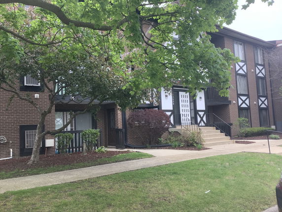 Front view of a multi-story brick residential building with white accents and a staircase leading to the entrance.
