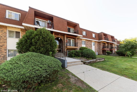 Front view of a multi-story apartment building with balconies and a brick facade.