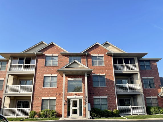 Front view of a three-story brick apartment building with balconies.
