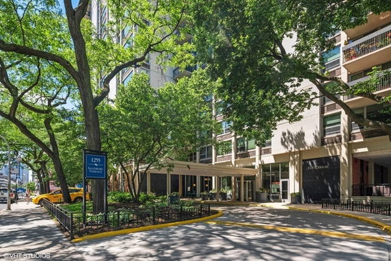 Front view of a multi-story building with a covered entrance and surrounding trees.