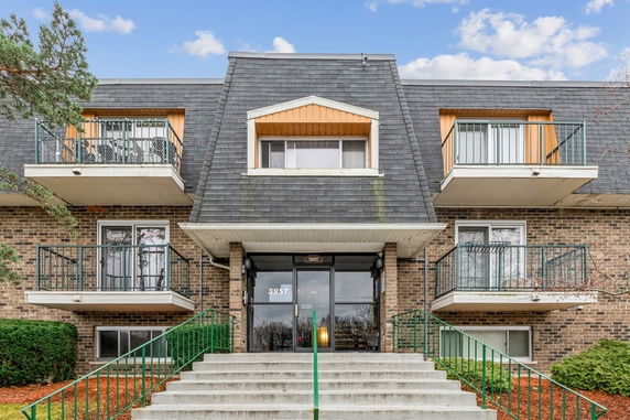 Front view of a brick apartment building with multiple balconies and a sloped roof.
