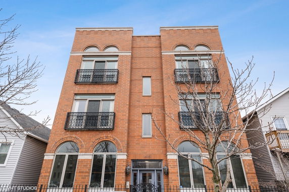 Front view of a three-story brick building with balconies and arched windows.