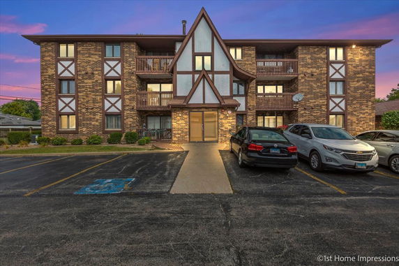 Front view of a multi-story brick building with balconies and a parking area.