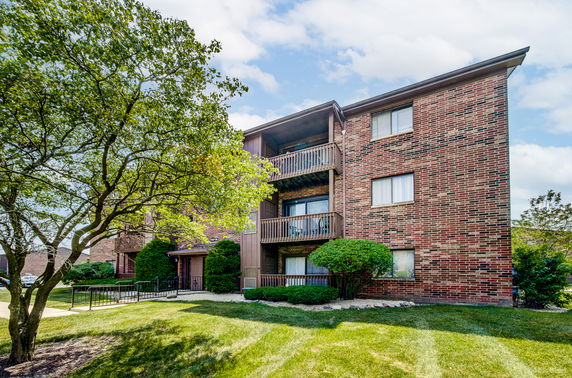 Front view of a three-story brick apartment building with balconies.