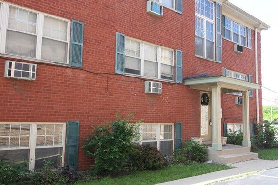 Front view of a brick apartment building with multiple windows and air conditioning units.