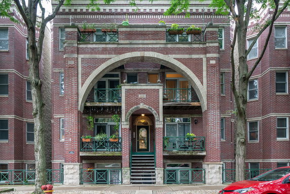 Front view of a brick apartment building with arched entrance and balconies.