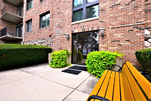 Front view of a brick building entrance with a glass door and surrounding greenery.
