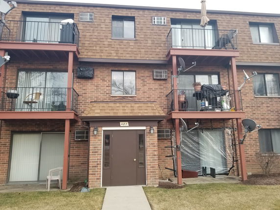 Front view of a multi-story brick building with balconies and satellite dishes.