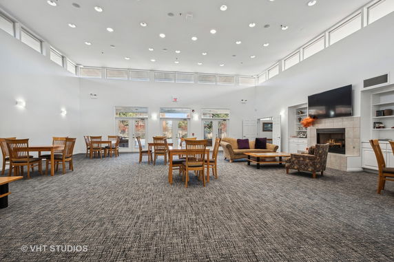 Spacious clubhouse interior with tables, chairs, and a fireplace.