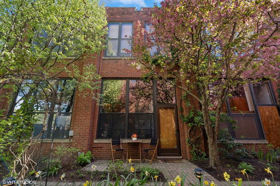 Front view of a brick building with large windows and a small patio area with chairs.