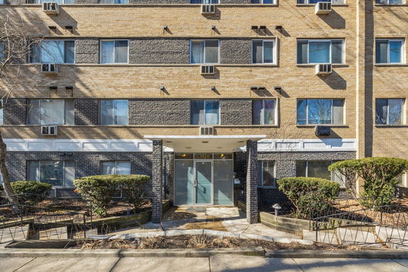 Front view of a multi-story brick apartment building with multiple windows and a central entrance.