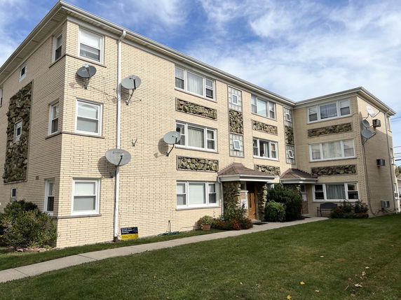 Front view of a three-story residential building with multiple satellite dishes.