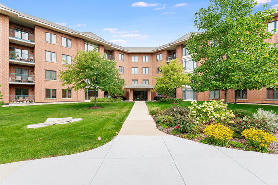 Front view of a multi-story brick building with balconies and landscaped entrance.