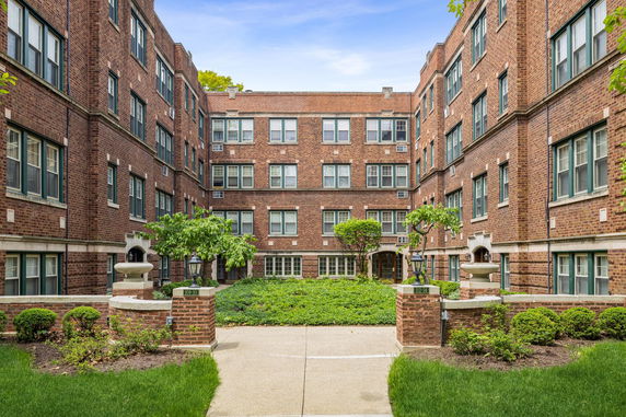Front view of a multi-story brick apartment building with landscaped courtyard.