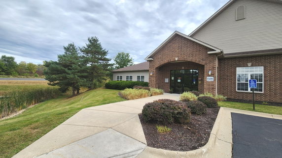 Front view of a brick building with an entrance, surrounded by landscaped greenery and a paved walkway.