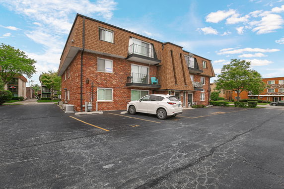 Front view of a three-story brick apartment building with balconies and parking area.