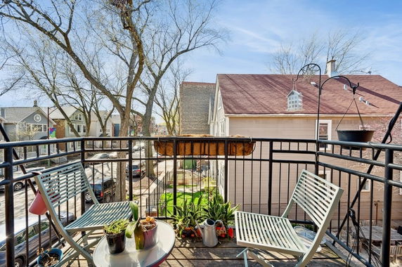 View from a balcony with chairs and plants, overlooking neighboring houses and trees.