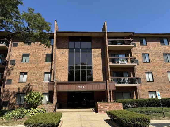 Front view of a brick multi-story apartment building with balconies and large windows.