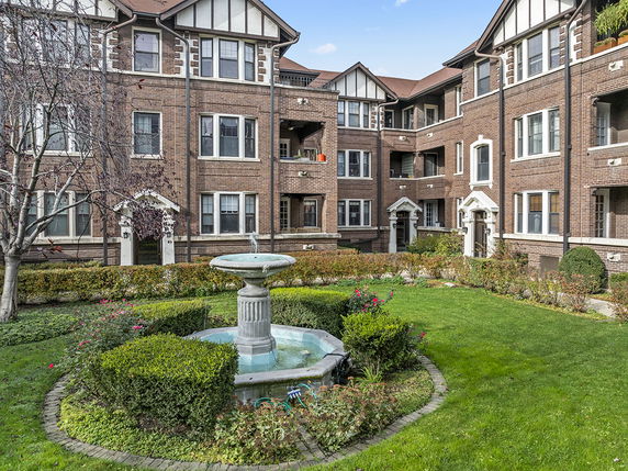 Front view of a multi-story brick apartment building with a central fountain and landscaped garden.