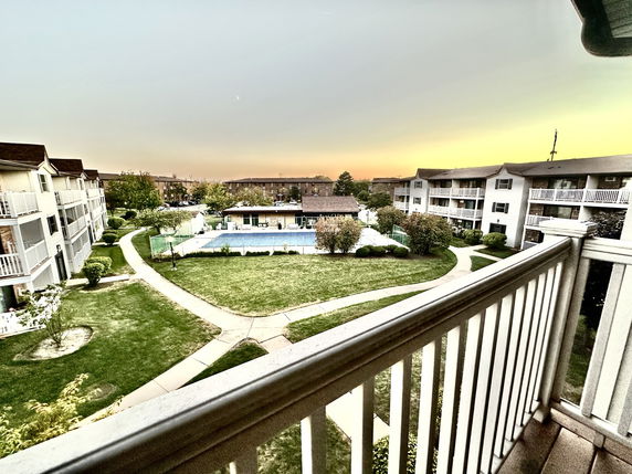 Panoramic view from a balcony overlooking apartment buildings and a central courtyard with pathways and a pool.