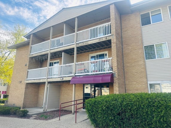 Front view of a multi-story residential building with balconies and an entrance with an awning.