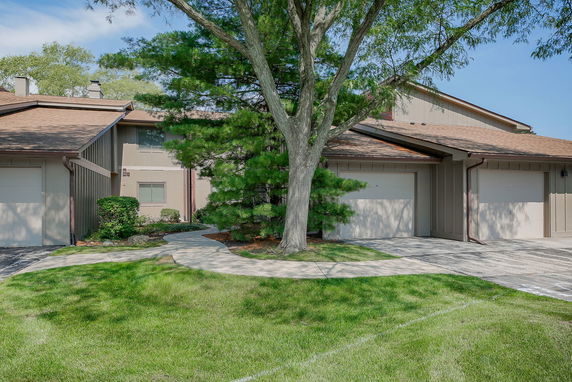 Front view of a house with adjacent garages and a tree.