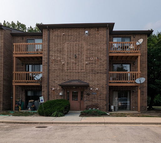Front view of a three-story brick building with balconies and satellite dishes.