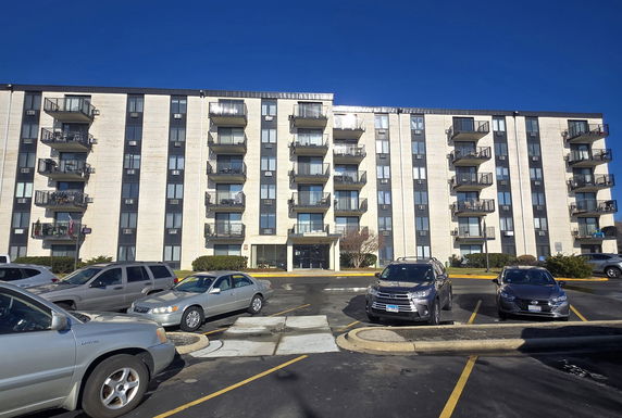 Front view of a multi-story apartment building with balconies and parking area.