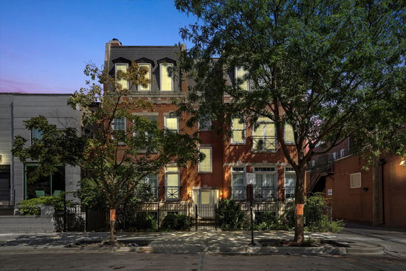 Front view of a three-story brick building with illuminated windows and trees in front.