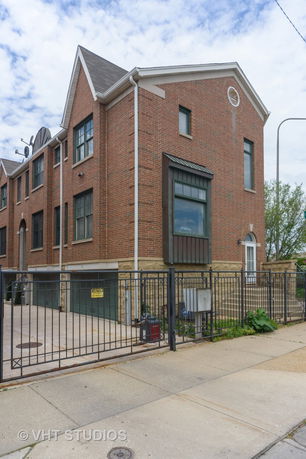 Front view of a multi-story brick house with large windows and a gated driveway.