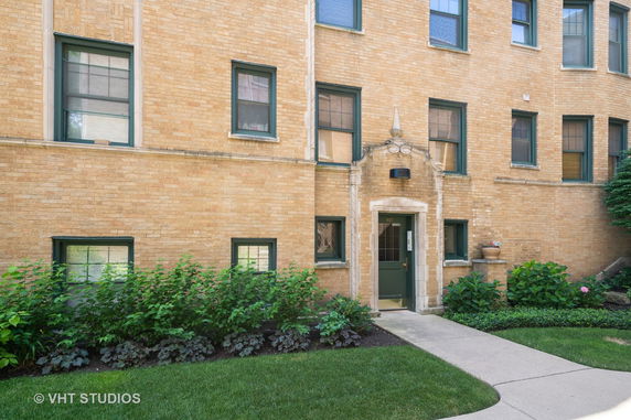 Front view of a multi-story brick building with green-framed windows and an entrance pathway.