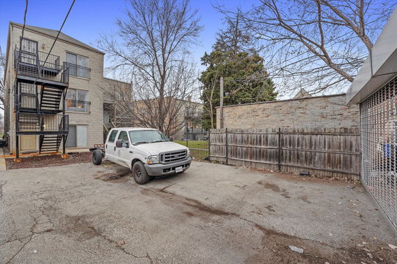 Outdoor parking area with a parked white truck beside a multi-story building with external staircases.