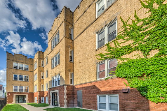Front view of a multi-story brick apartment building with ivy growing on the wall.