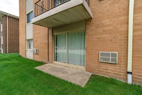 Exterior view of a building with a brick facade and sliding glass doors leading to a concrete patio.