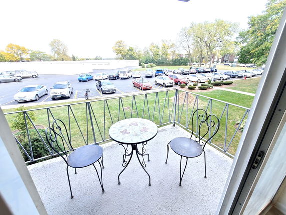 View from a balcony overlooking a parking area with several cars and greenery.