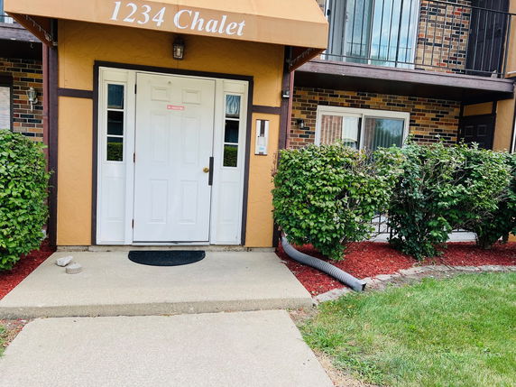 Front view of a small apartment building entrance with a white door and brick facade.