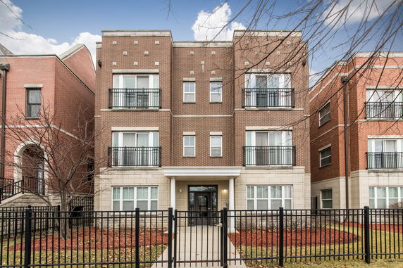 Front view of a multi-story brick apartment building with balconies and a black fence.