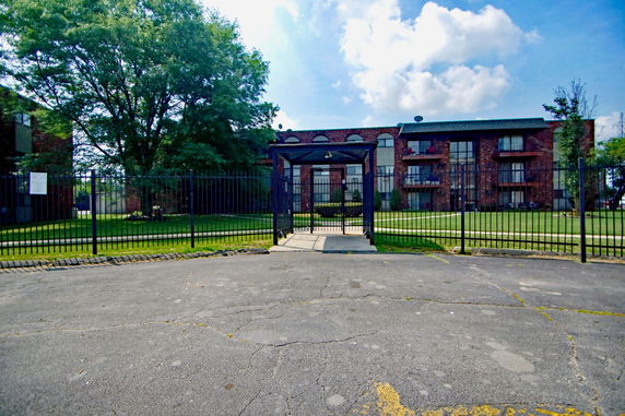 Front view of a multi-story brick building with balconies and surrounded by a fence.
