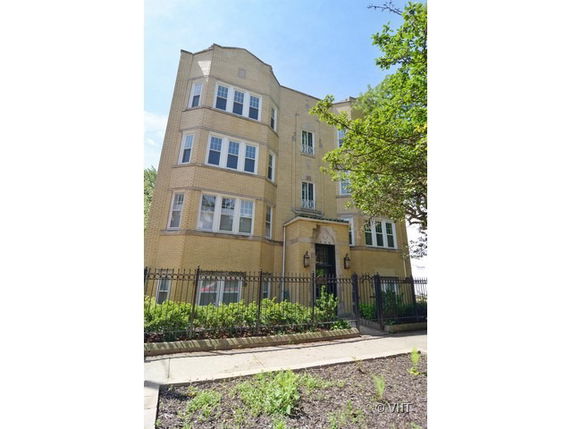 Front view of a multi-story apartment building with a fenced entrance.